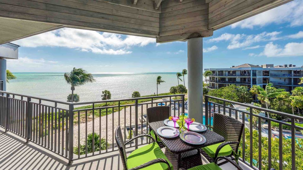 A wide angle picture of a condo's porch in Key West. A table and chairs are in the foreground, and the view looks out to the ocean. 